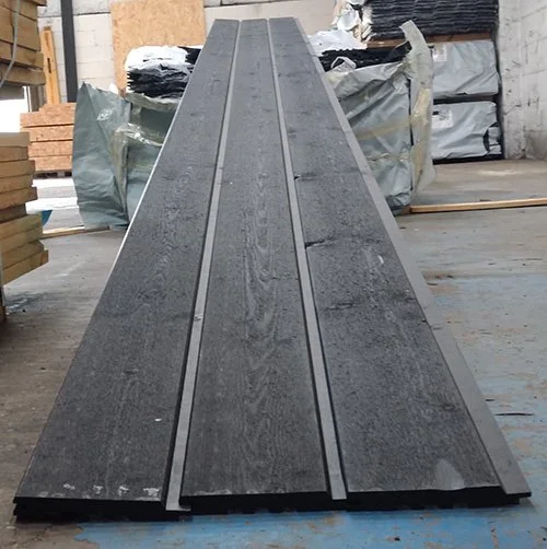 Long gray wooden board with grooves, lying flat on a concrete floor in a warehouse or construction site.