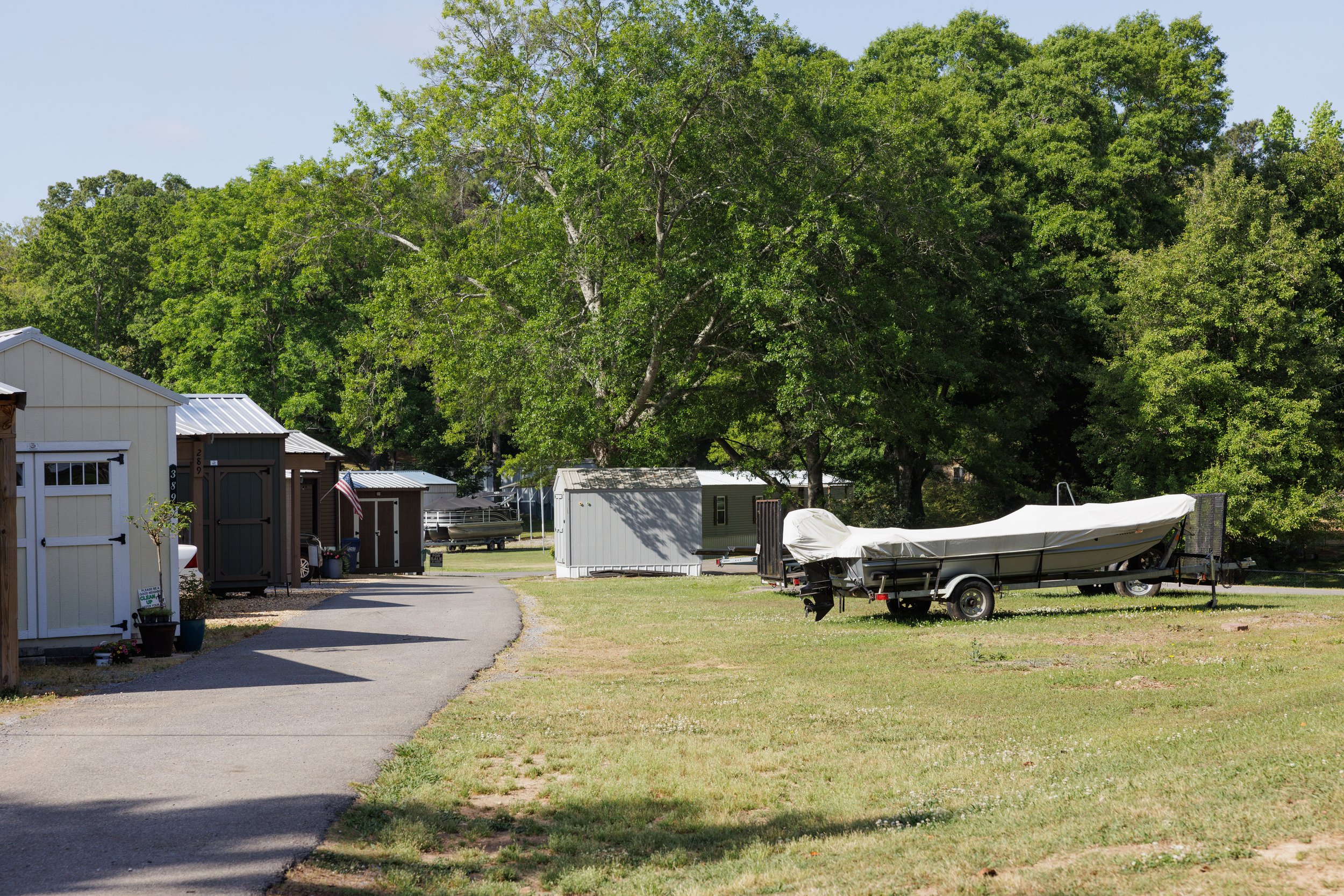 Small outdoor storage area with white shed, boat, and trees in the background.