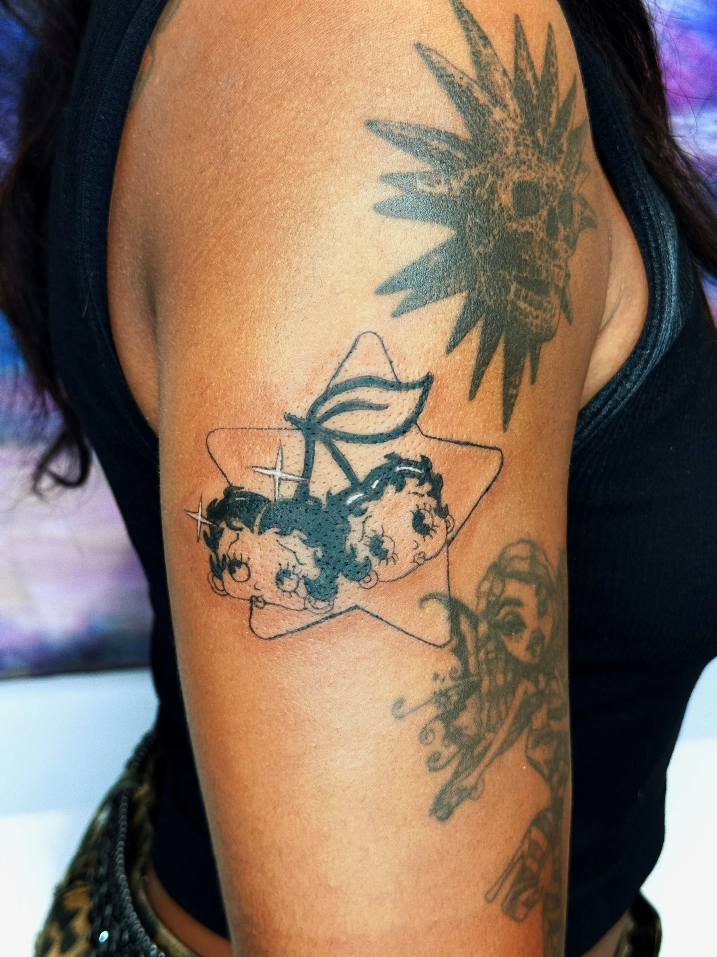 Tattoo of a skull with flowers and leaves inside a geometric frame on upper arm.