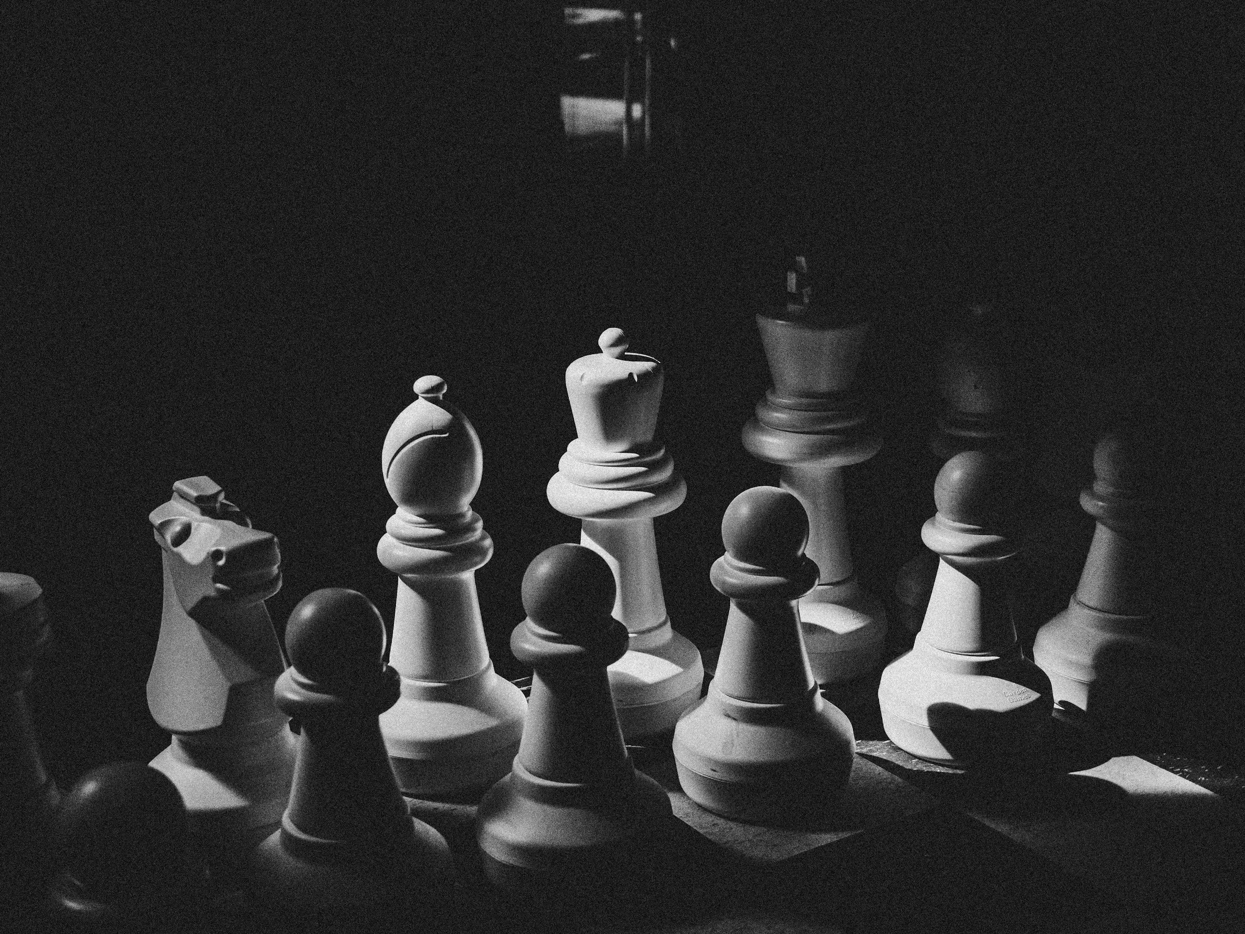 Black and white photograph of a chessboard with chess pieces in play, including pawns, rooks, a knight, and a queen, set up for a game.