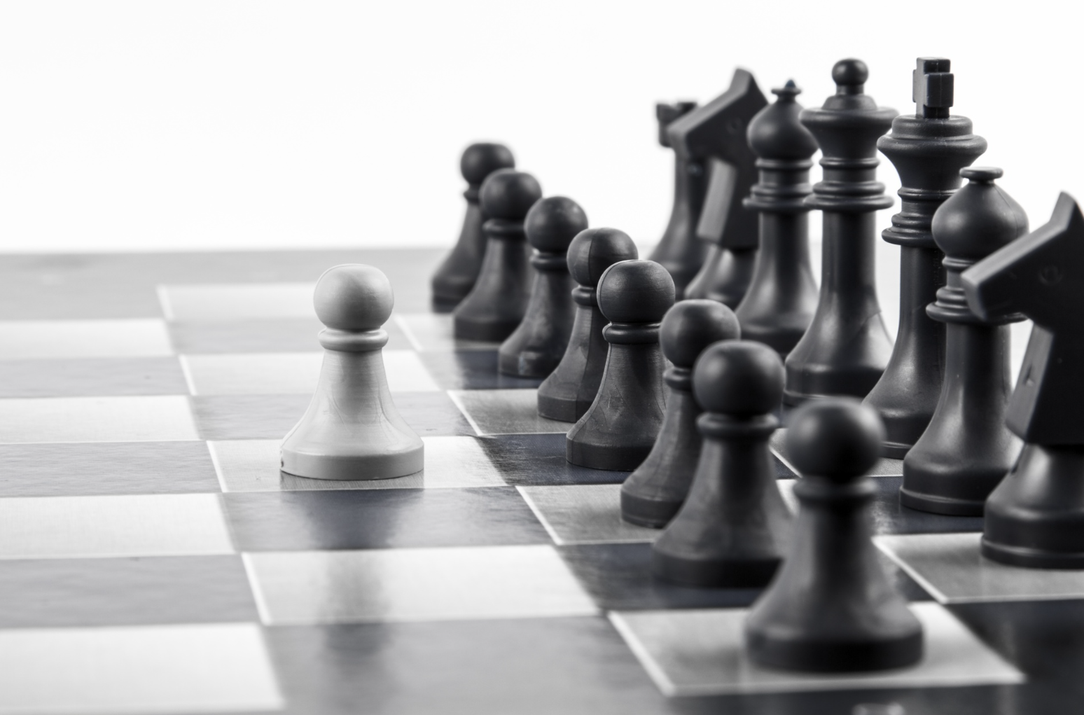 Black and white chessboard with chess pieces, with a white pawn in the foreground and the rest of the black pieces behind it.