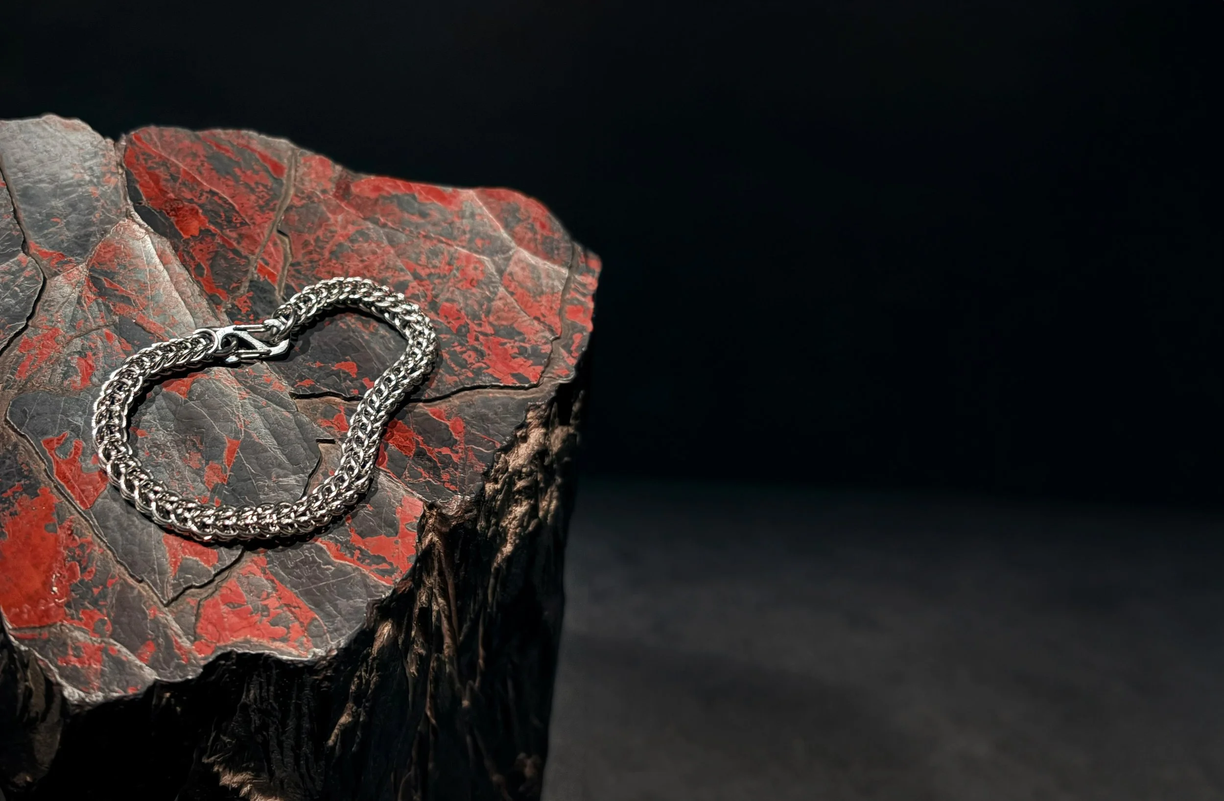 Silver braided chain necklace resting on a cracked, dark red and gray stone slab against a black background.