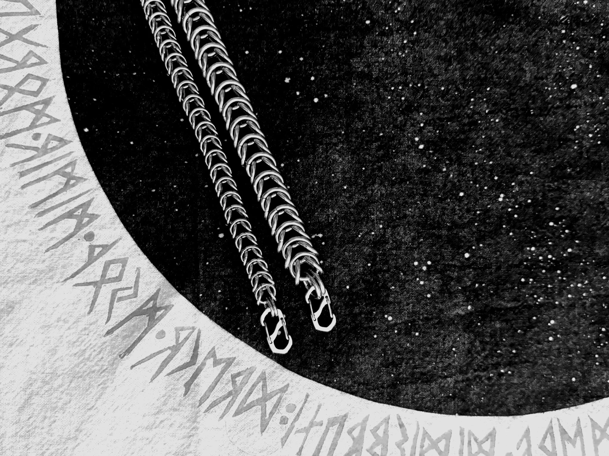 Two silver chains on a black fabric background with a white circular border with inscriptions.