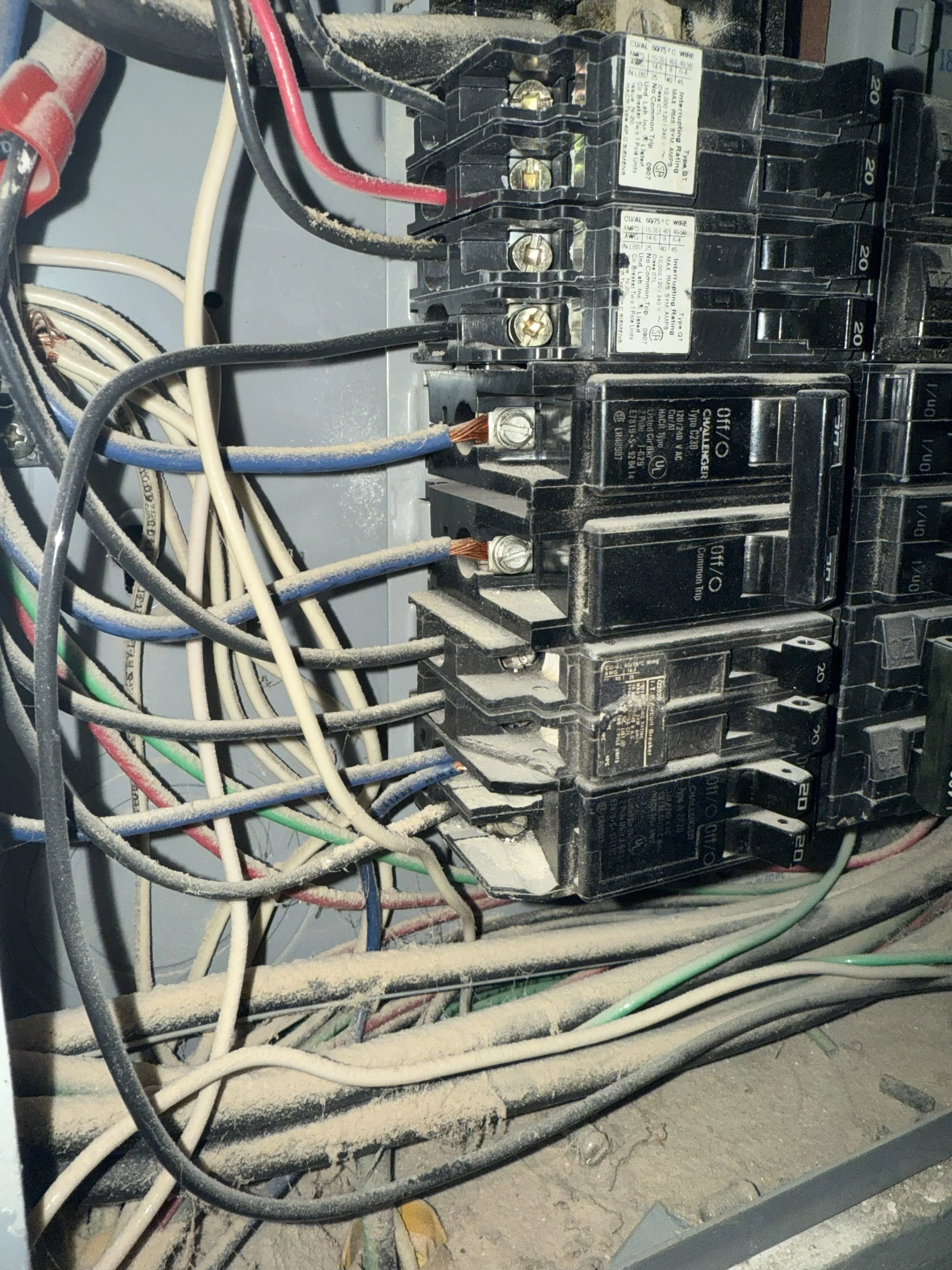 A dusty electrical breaker box with multiple wires and circuit breakers.