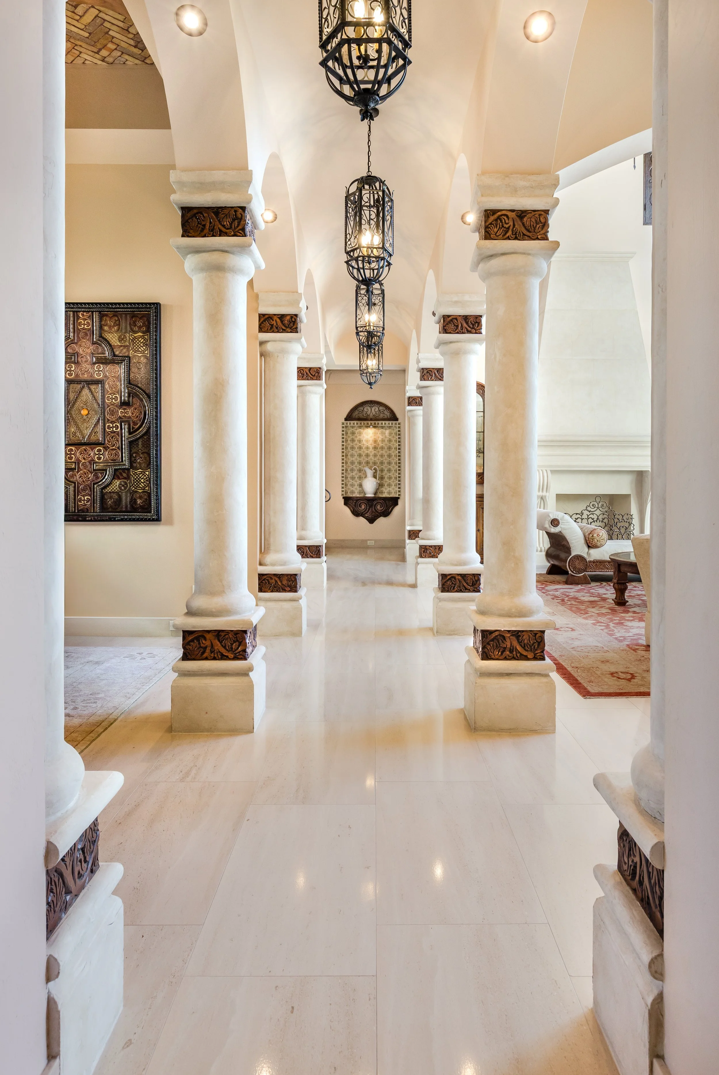 An elegant hallway with tall, white columns and intricate dark wood accents, decorated with ornate chandeliers hanging from the ceiling.