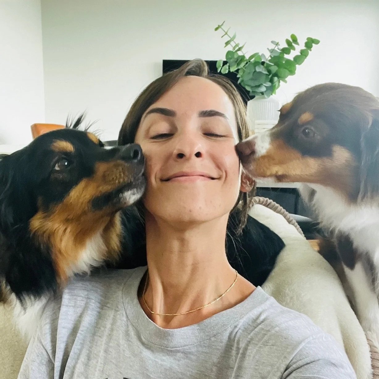 Woman smiling with two dogs licking her face.