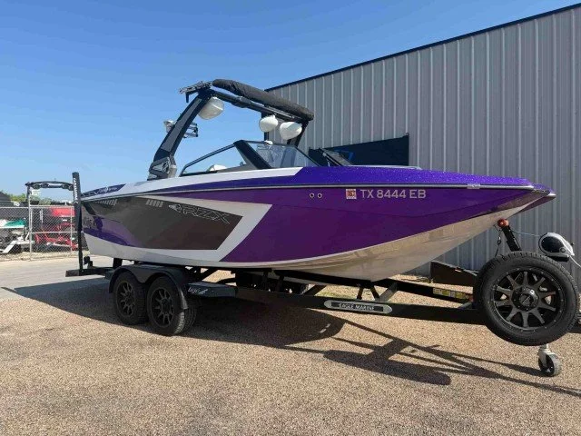 Purple and black speedboat on a trailer with a gray building in the background.