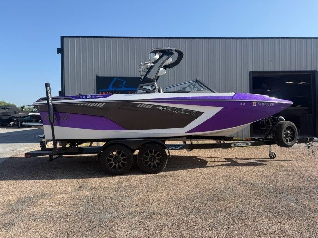 A purple and white speedboat on a dual-axle trailer parked outside near a large metal building