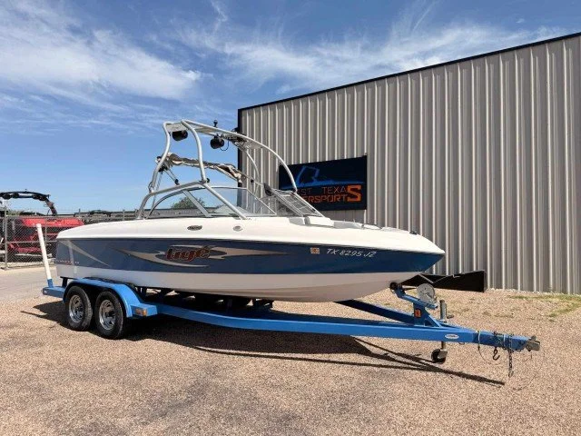 White and blue speedboat on a blue trailer parked outside a metal building on a sunny day.