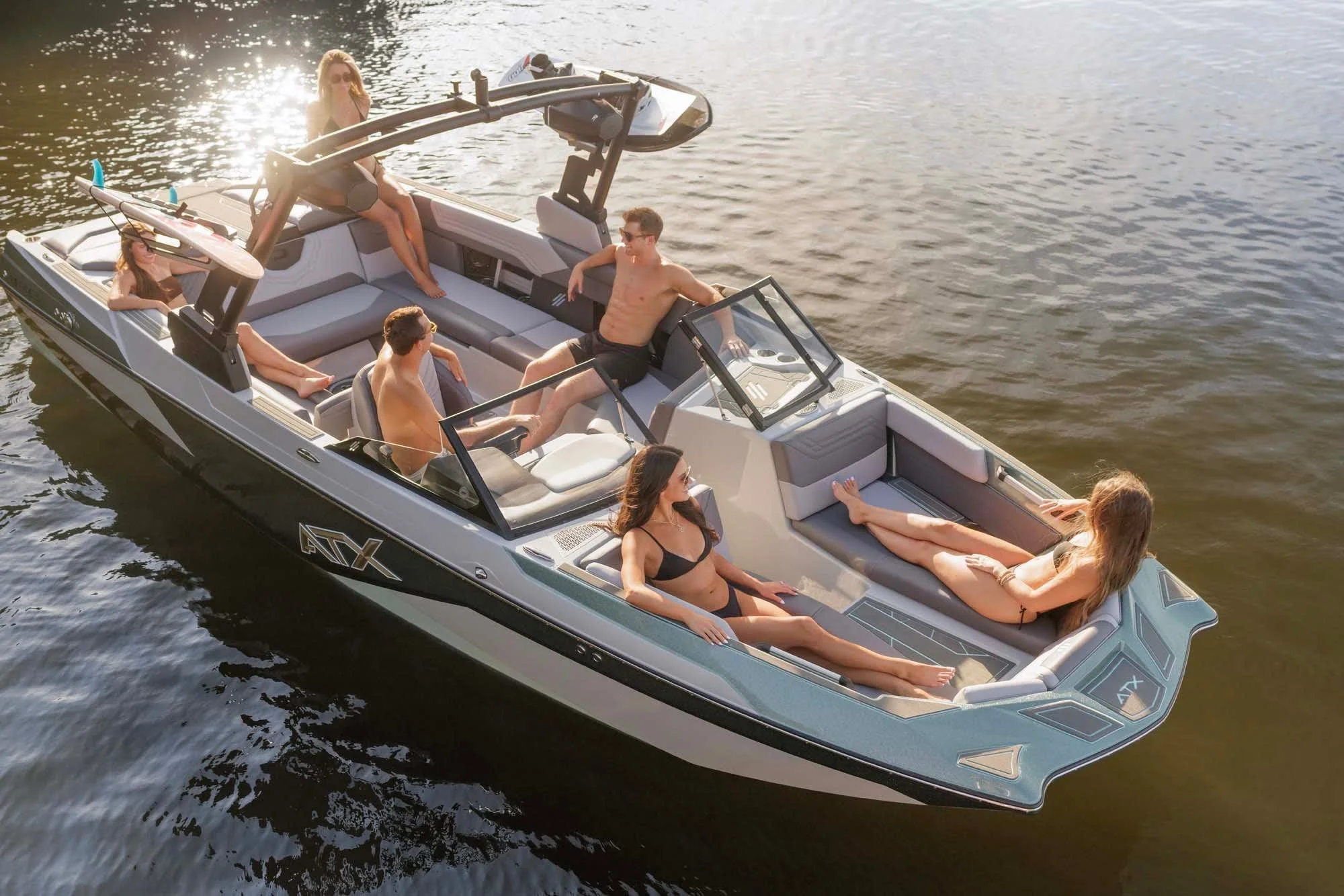 Six people in swimsuits relax and chat on a boat floating on calm water under bright sunlight.