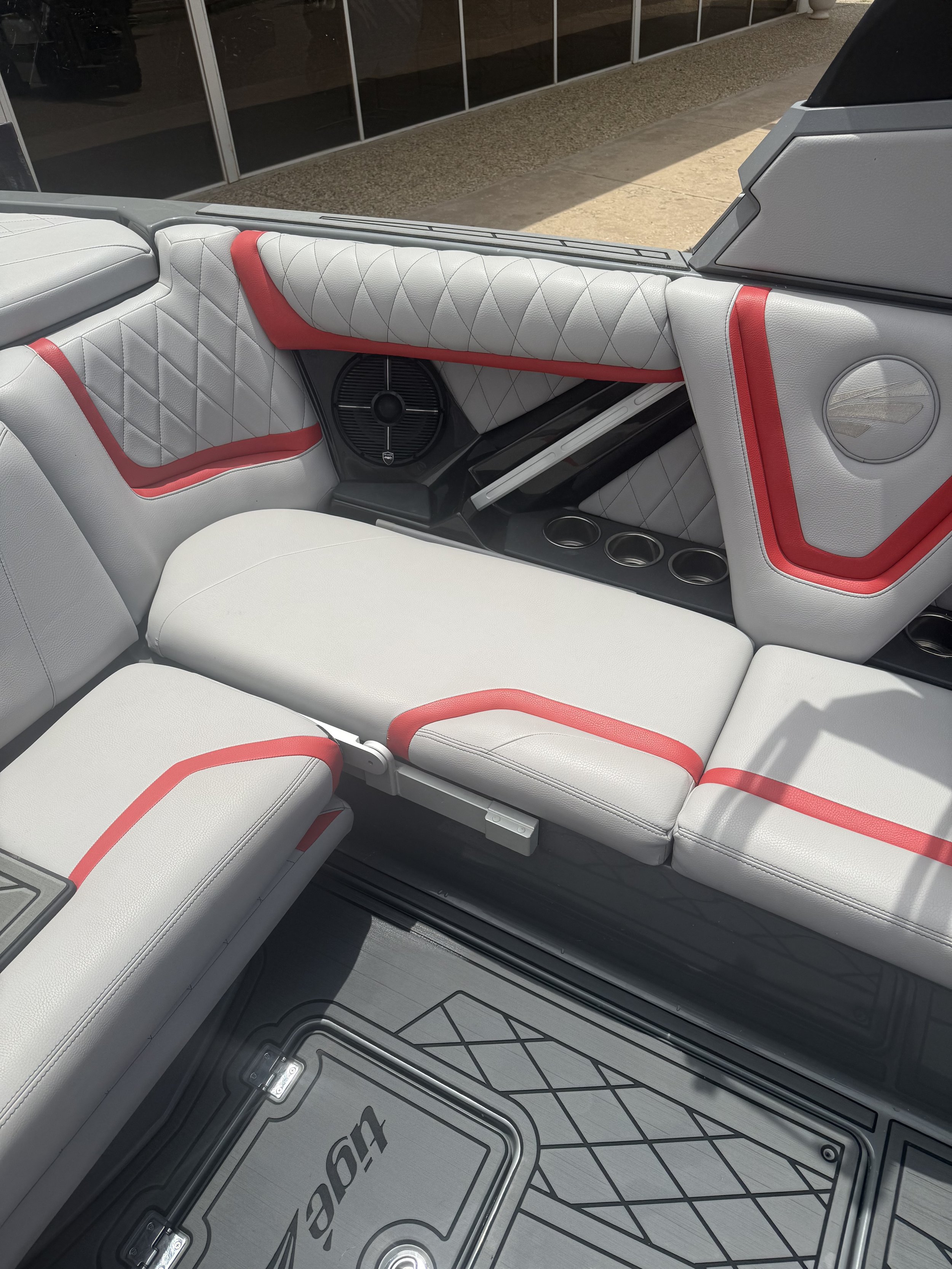Interior of a boat with white cushioned seats and red accents, silver and black speaker, and a floor with diamond and geometric patterns.