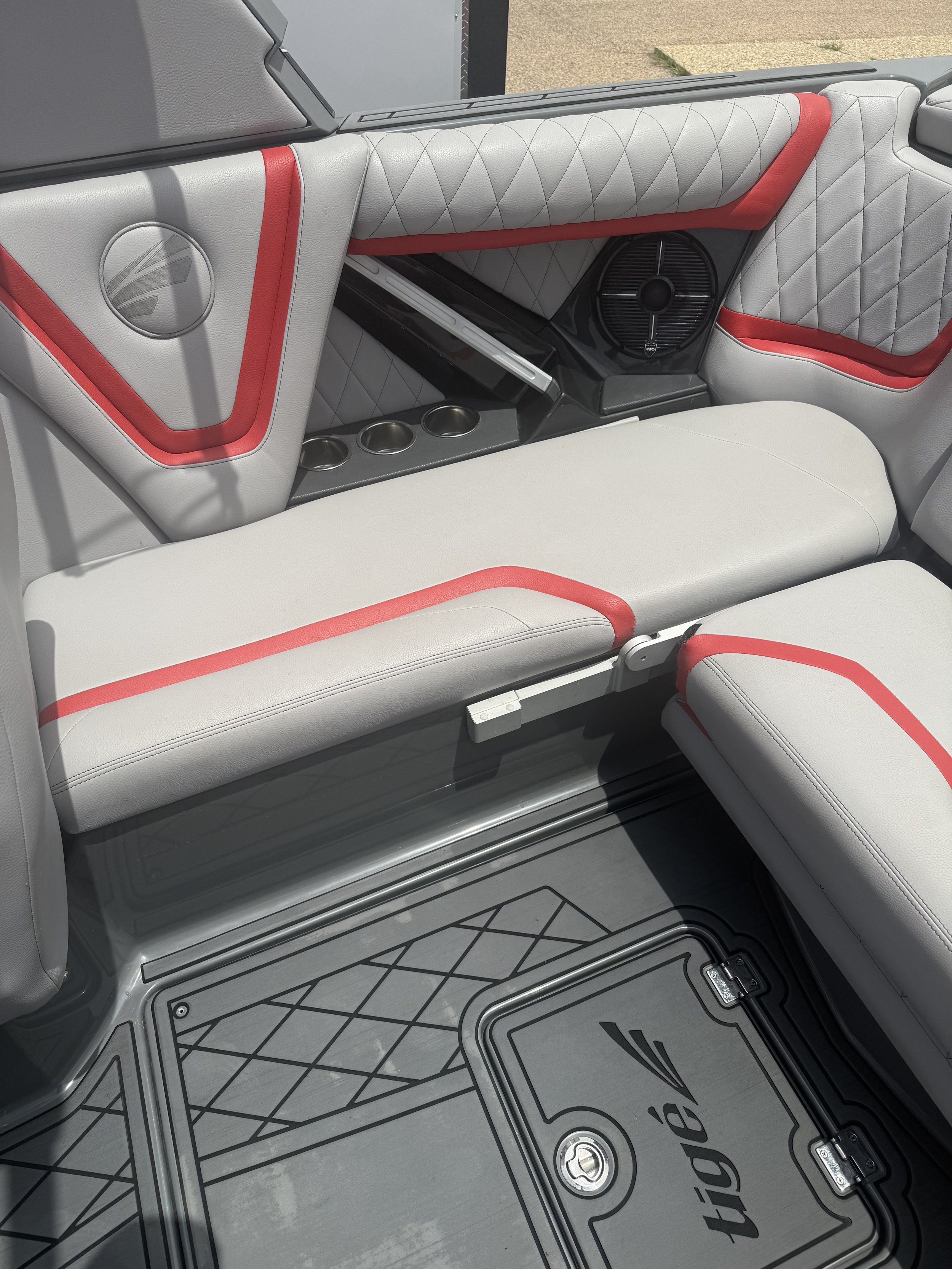 Interior of a boat with white and red cushioned seating, a built-in speaker, a magazine holder, four cup holders, and a rubber floor mat with a geometric pattern and logo.