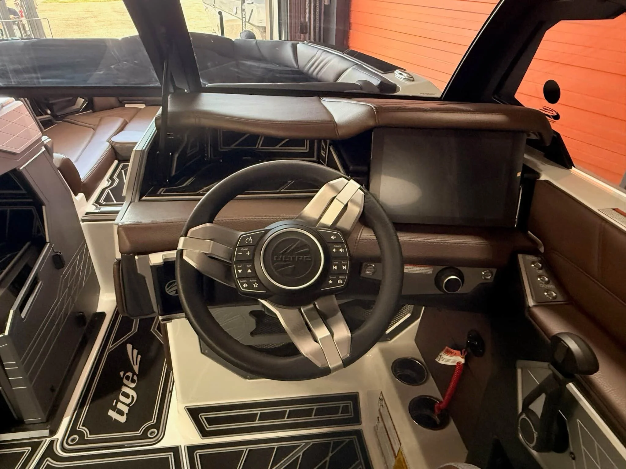 The image shows the interior of a vehicle, focusing on the dashboard, steering wheel, and front seat area with a black leather seat and various controls and buttons around the steering wheel.