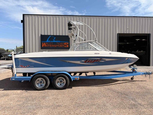 A speedboat on a trailer parked outside a building with a sign that reads 'West Texas Water Sports'.