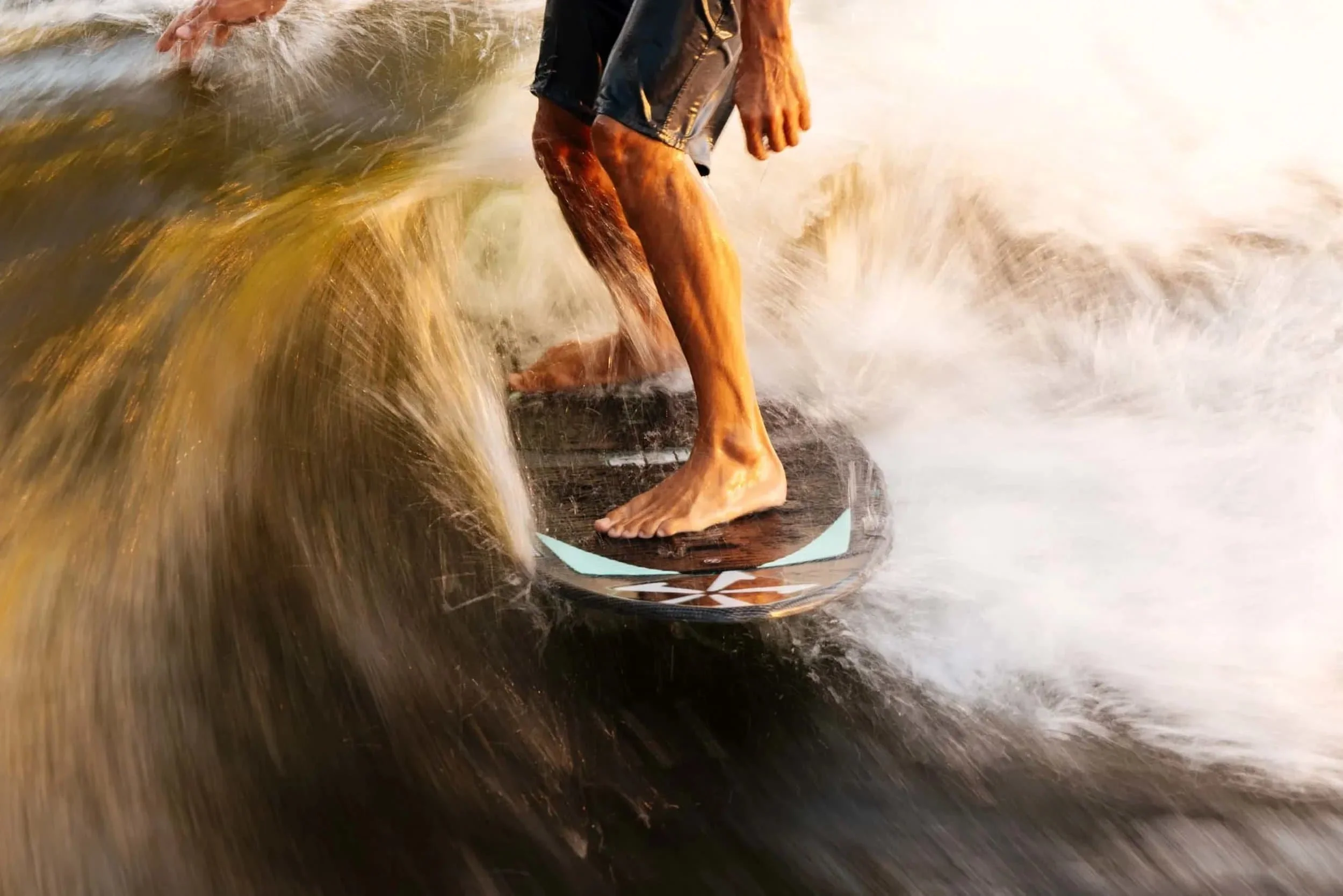 Close-up of a person surfing on a wave, standing barefoot on a surfboard with water splashing around.