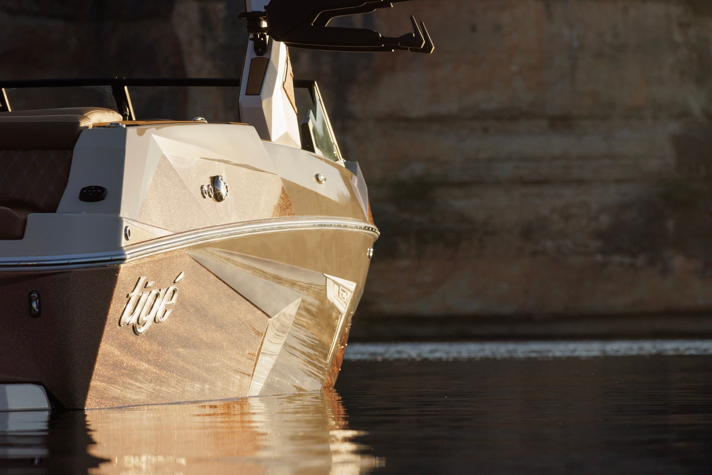 Close-up of the front side of a Tige boat floating on calm water, with a stone wall in the background.