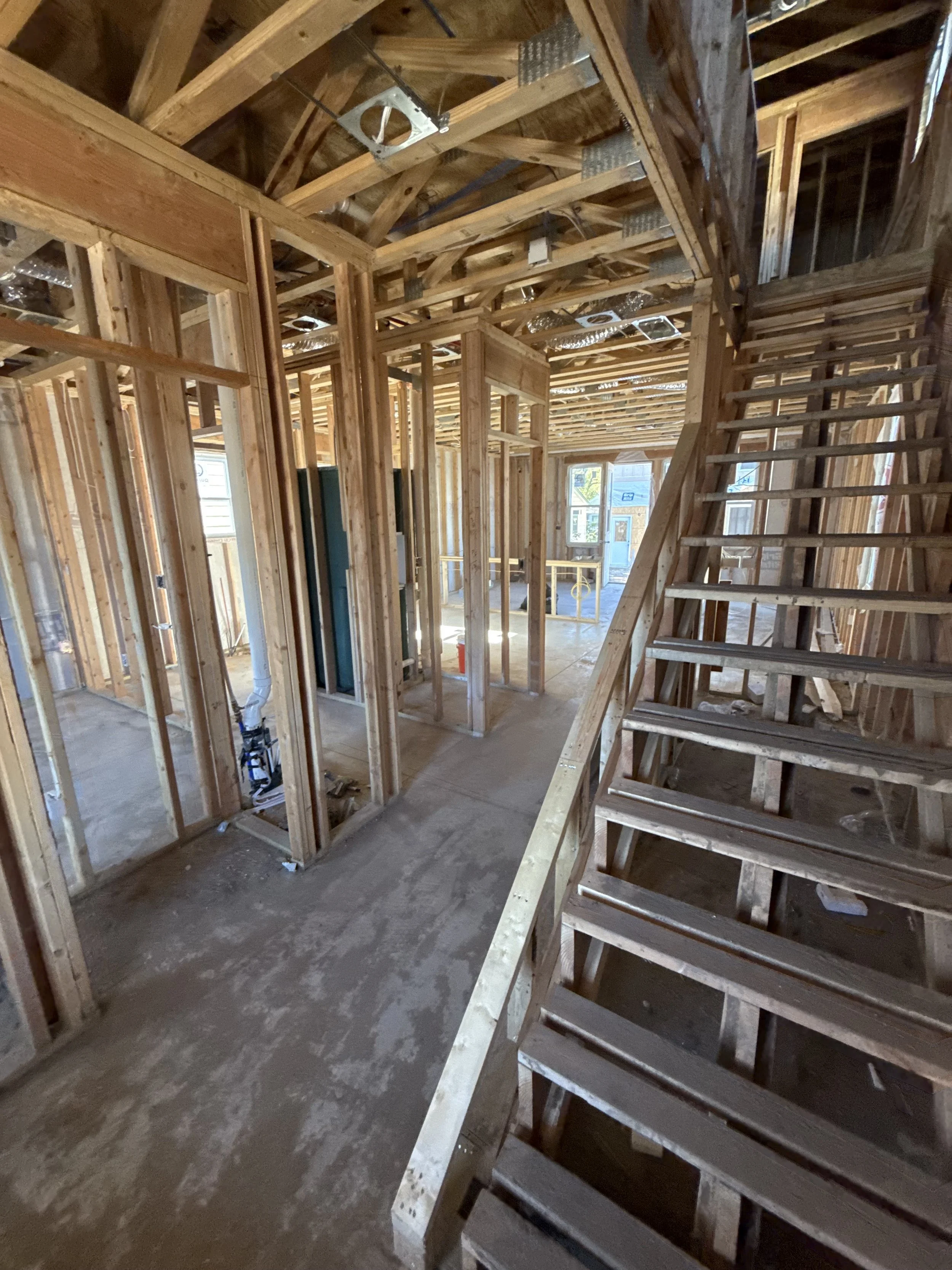 Interior of a house under construction with exposed wooden framing, staircase, and unfinished floors.