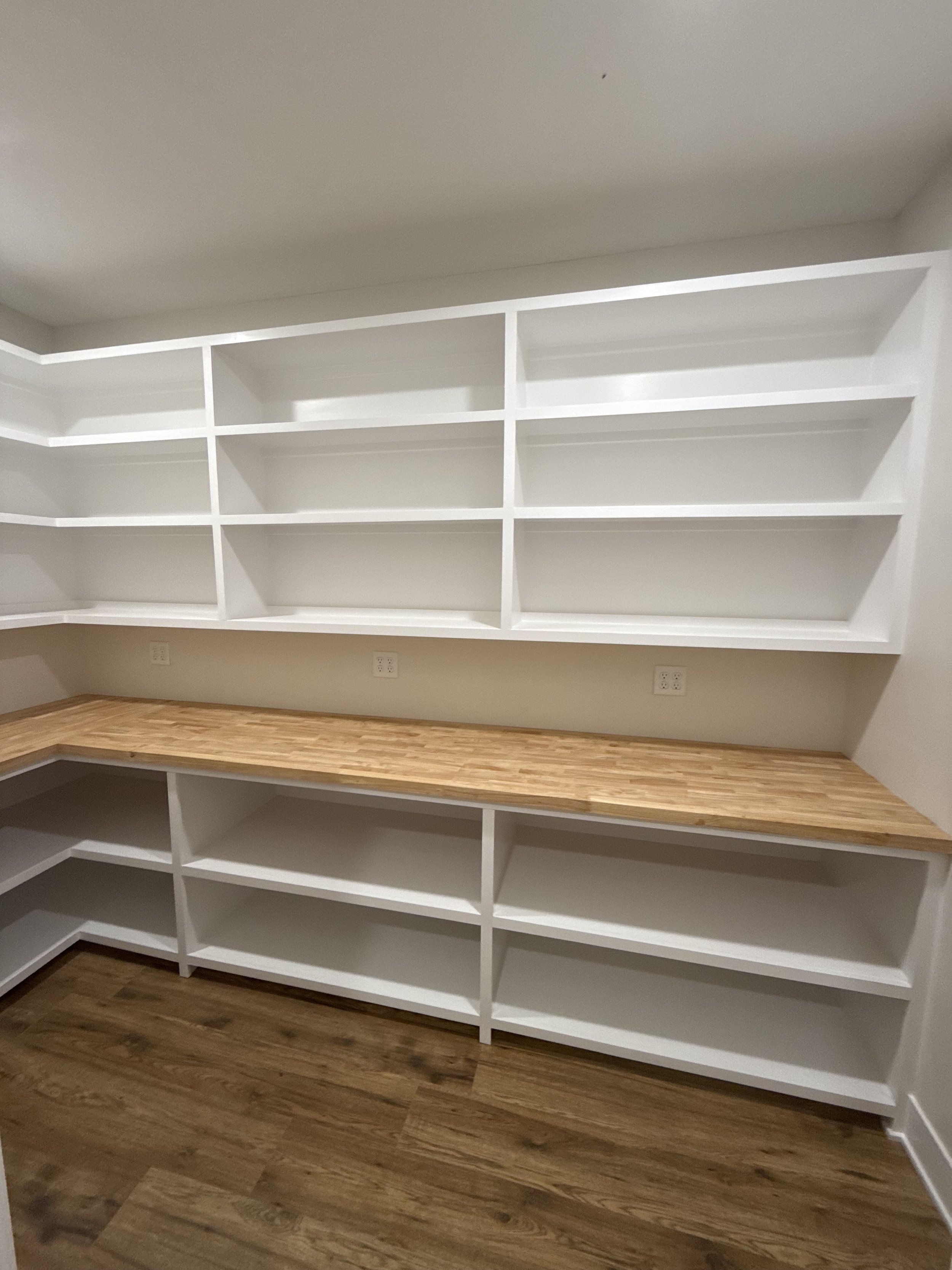 Empty white built-in shelves and lower cabinets with a wooden countertop in a room with wood flooring.
