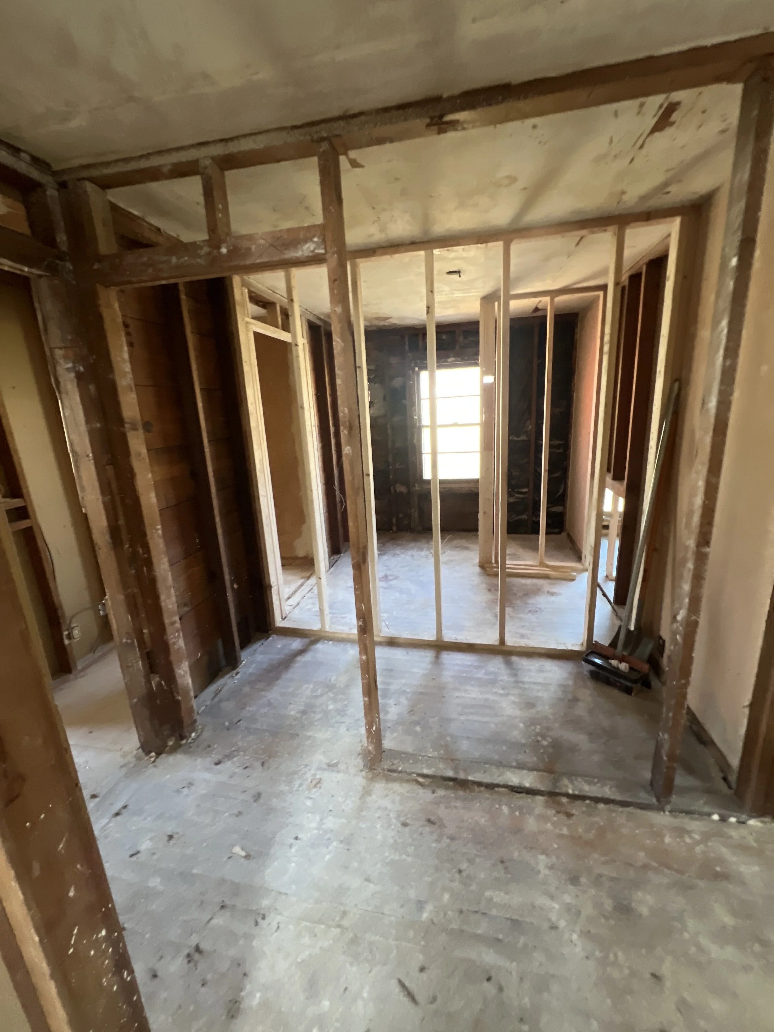Interior of a house under renovation with exposed wooden framing and a window in the background.