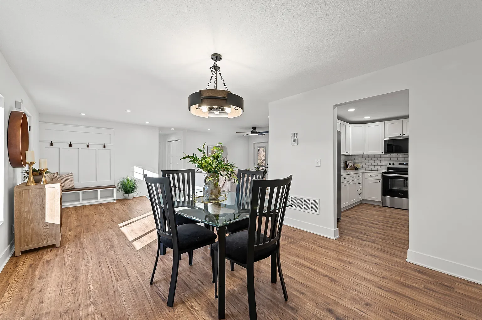 Open-concept living and dining area with a wooden floor, white walls, a black dining table with six black chairs, and a kitchen with white cabinets and stainless steel appliances.