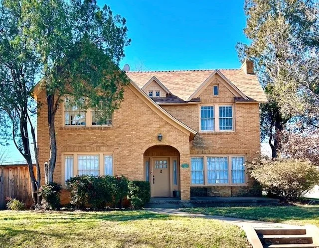 Two-story brick house with large windows, a central front door, and trees on both sides, under a clear blue sky.