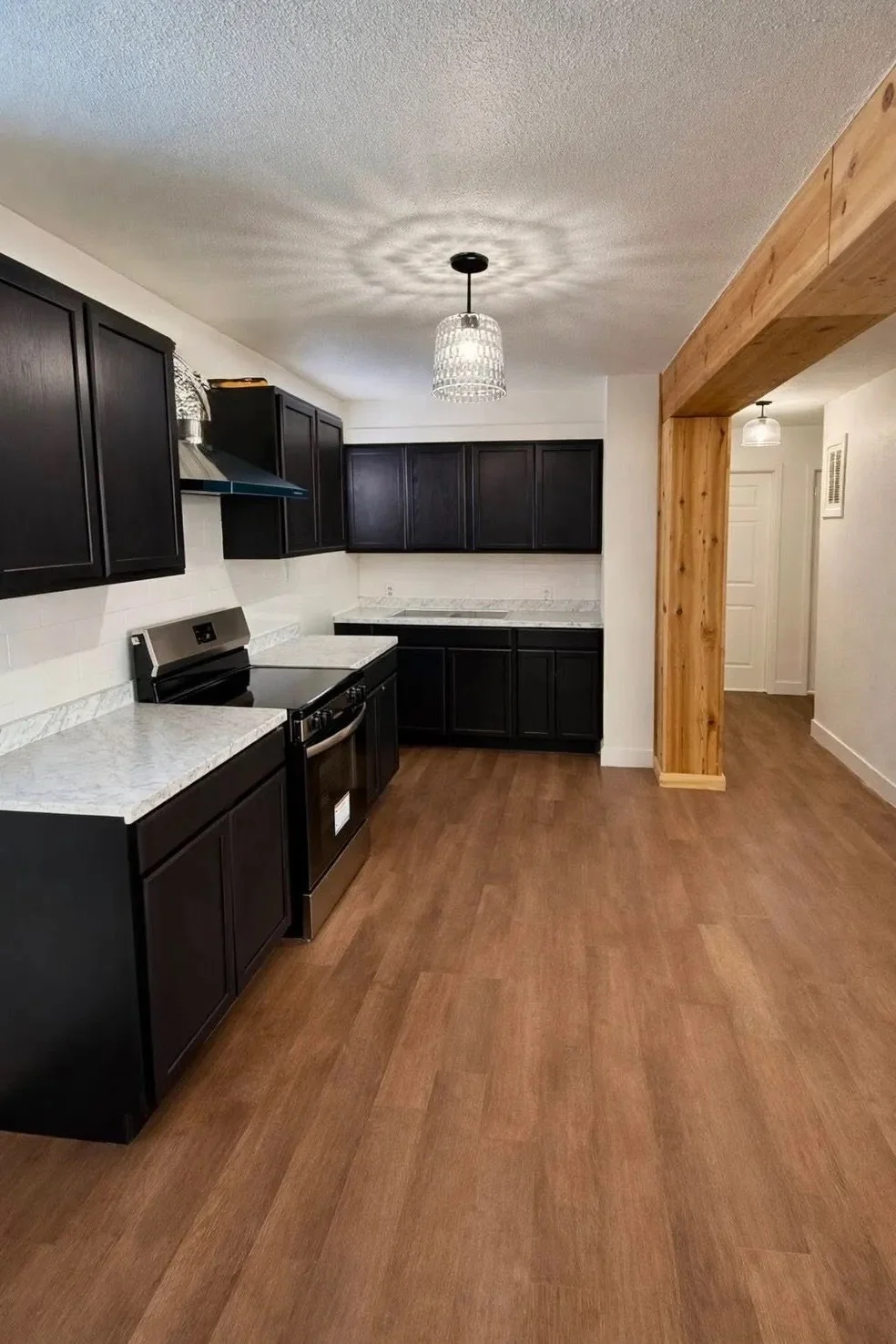 Modern kitchen with black cabinets, white marble countertops, black stove, wood flooring, and a wooden accent wall section.