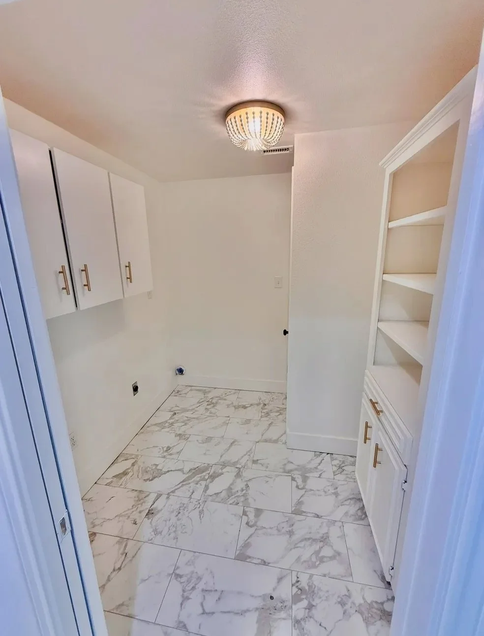 Empty laundry room with white cabinets, marble tile flooring, and a ceiling light.