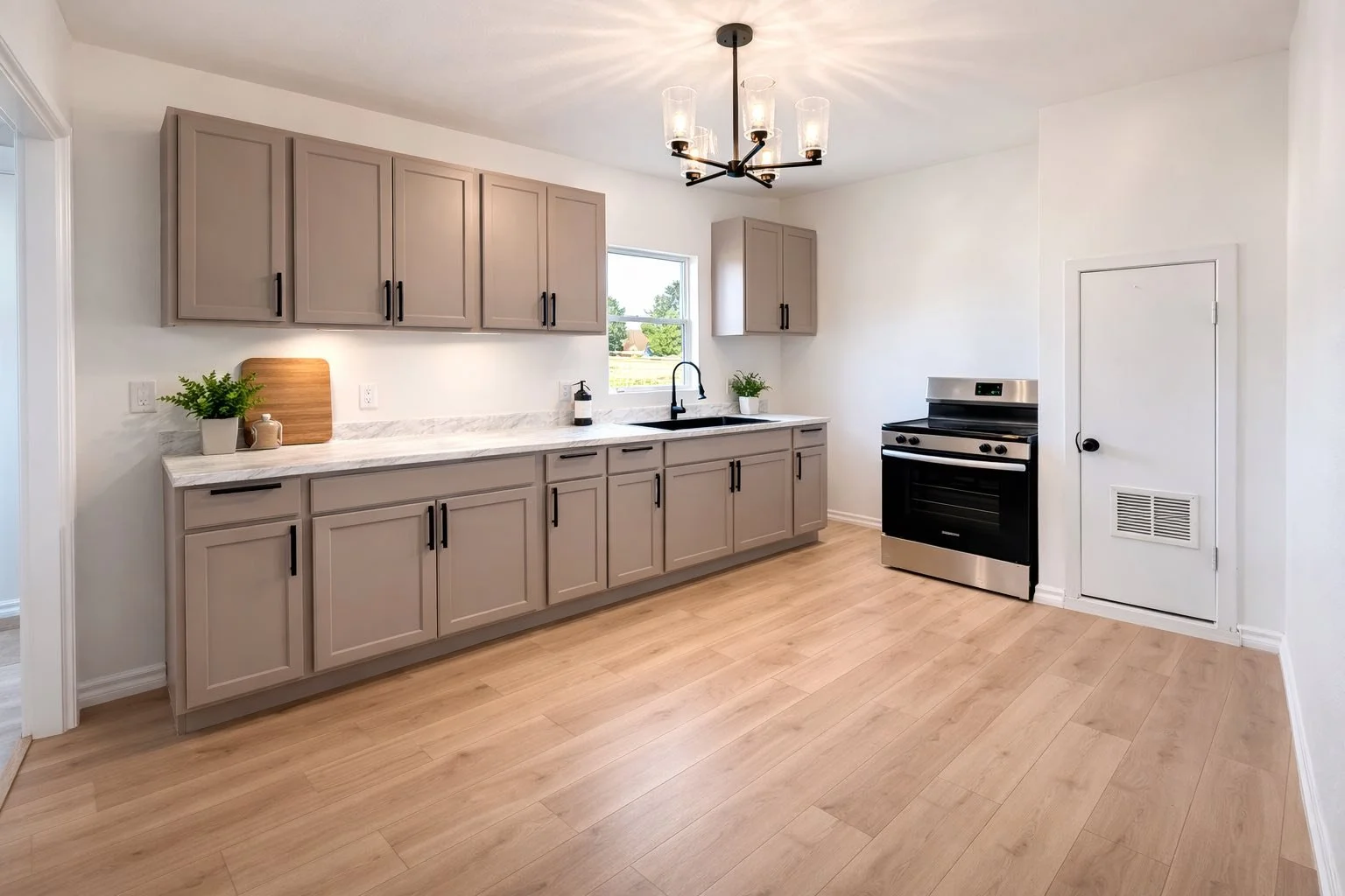 Modern kitchen with light wood floors, taupe cabinets, marble countertop, stainless steel stove, and a window above the sink.