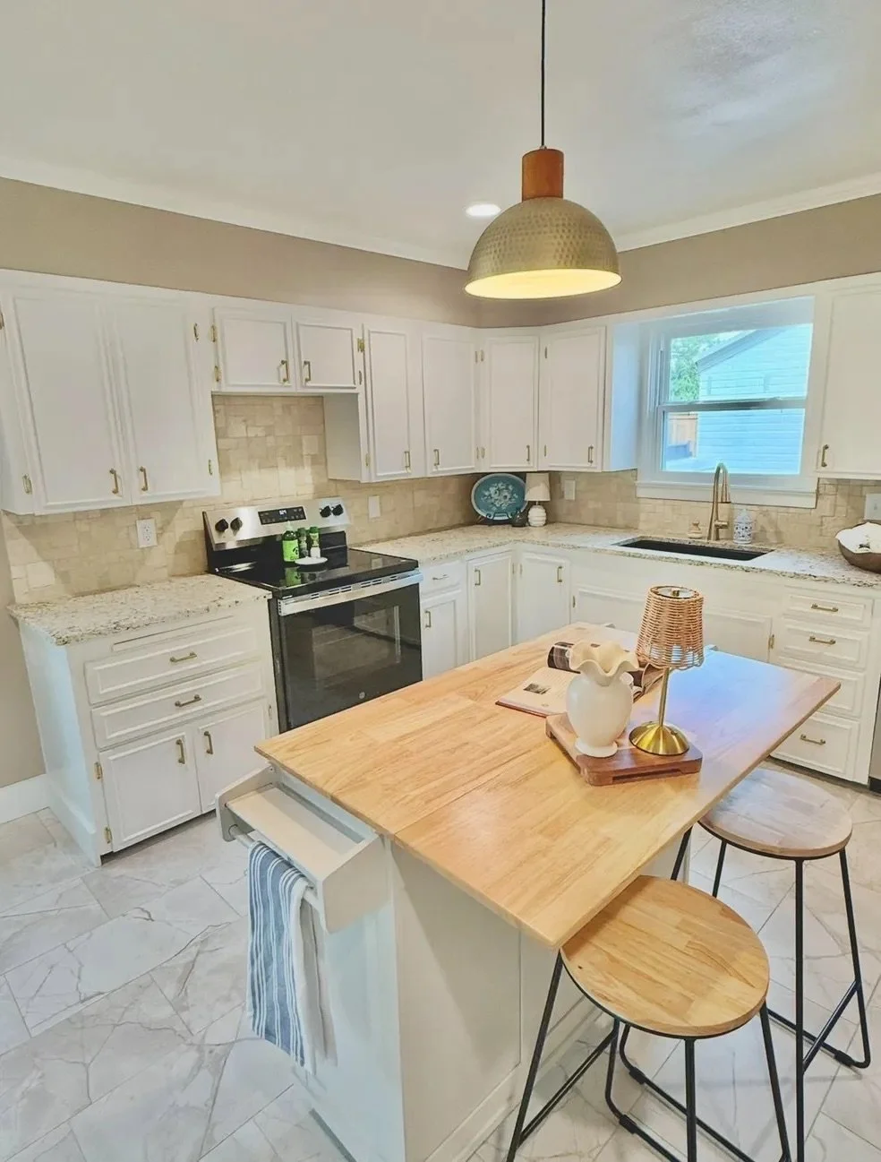 Kitchen with white cabinets, black oven, granite countertops, and a wooden island with two barstools.