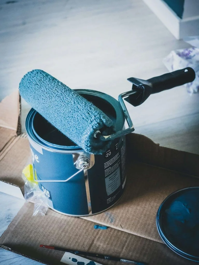 A blue paint roller rests on an open can, with painting supplies nearby—perfect for painting services in Abilene, TX.