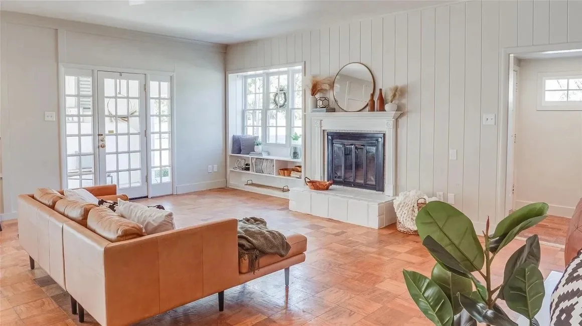 Bright living room with parquet floors, tan sofa, fireplace, large windows, and glass doors; modern, cozy decor with plants.