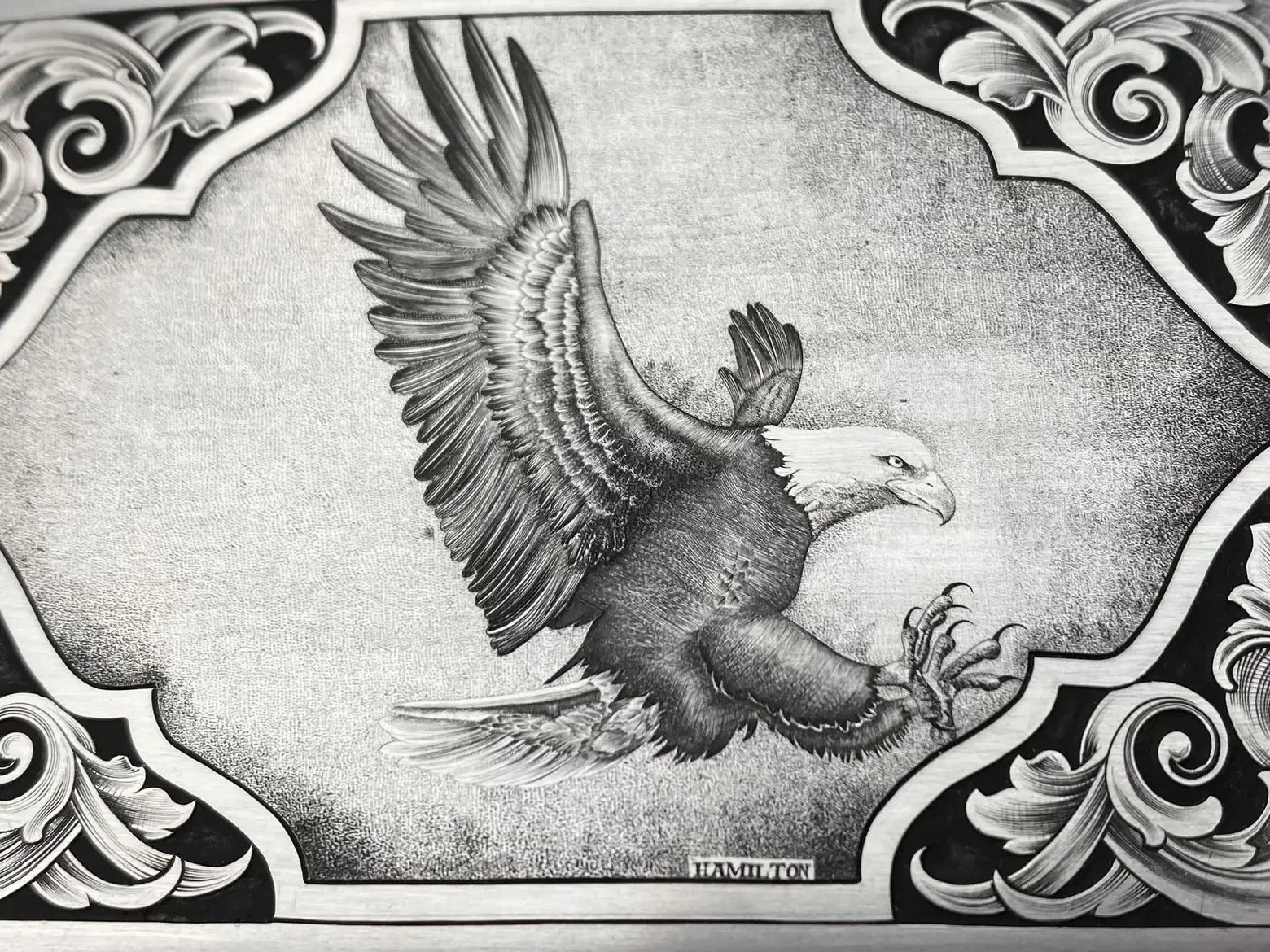 Close-up of hand-engraved bulino style Bald eagle with American scrollwork on stainless steel belt buckle.