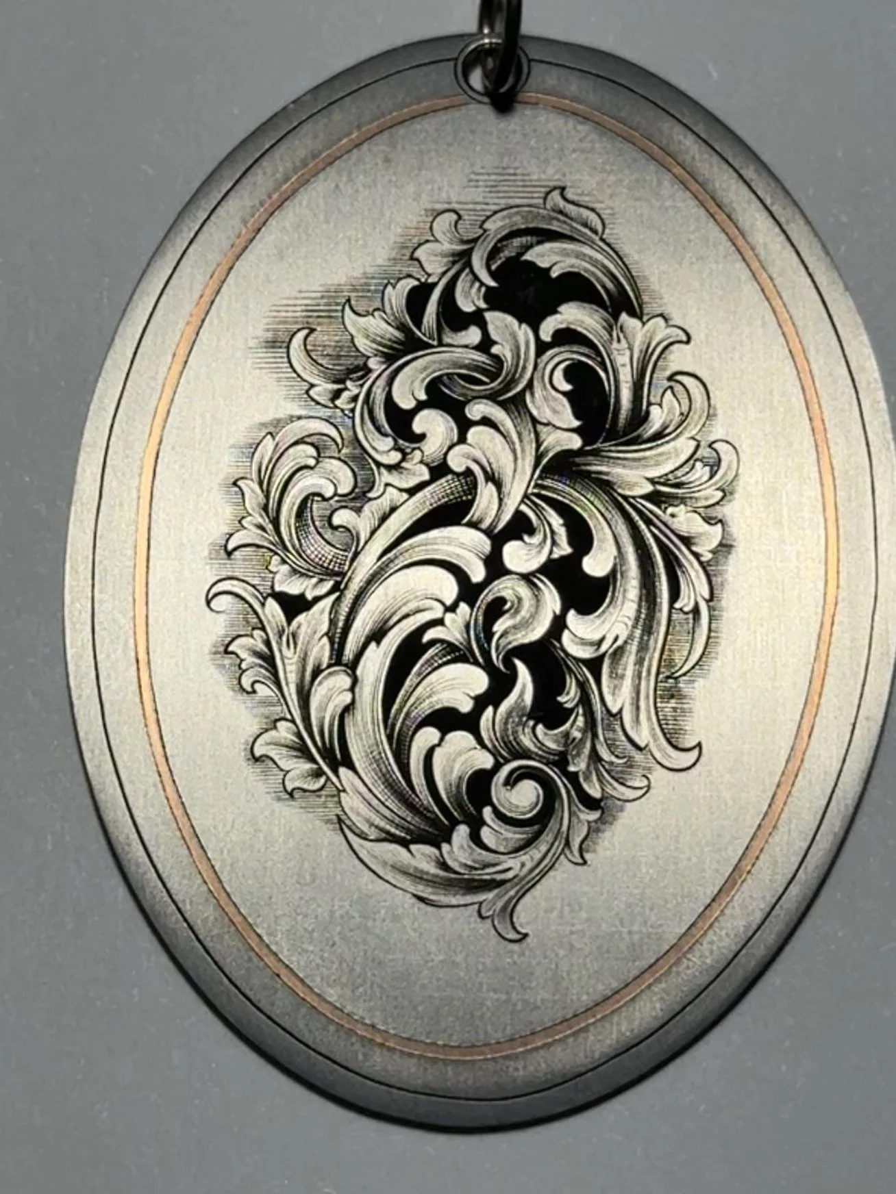 Close-up of hand-engraved American Scrollwork on a titanium pendant.