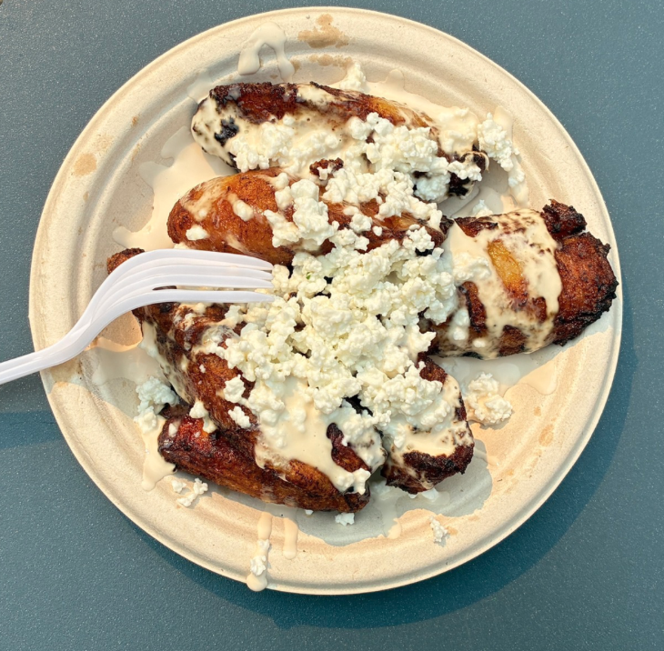 Plate of fried chicken drumsticks topped with white crumbles, possibly cheese, and drizzled with white sauce, with a plastic fork resting on the plate.