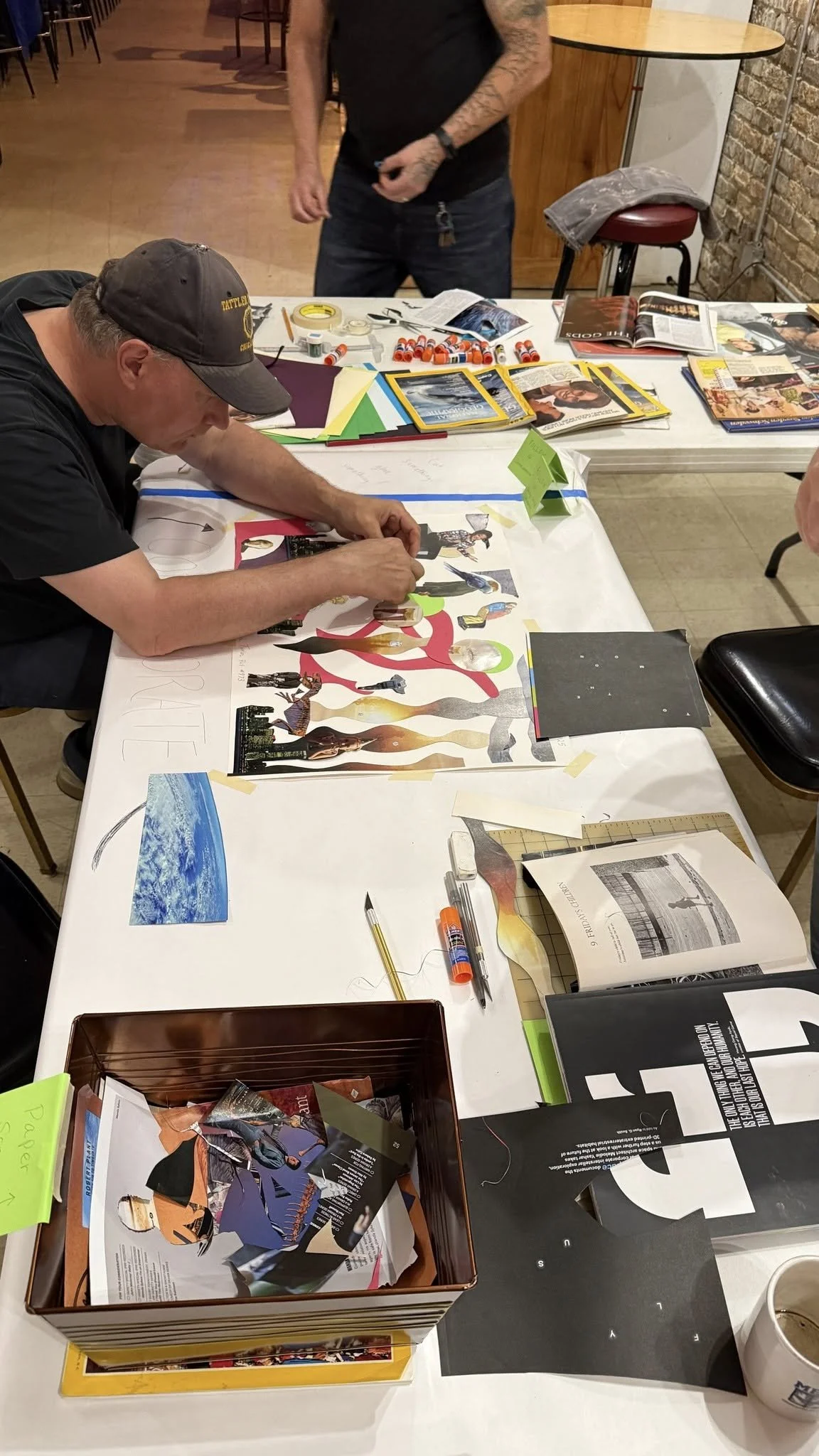 Veterans working on a collage or visual art project with magazines, paper cutouts, glue, and scissors on a table in a casual setting.