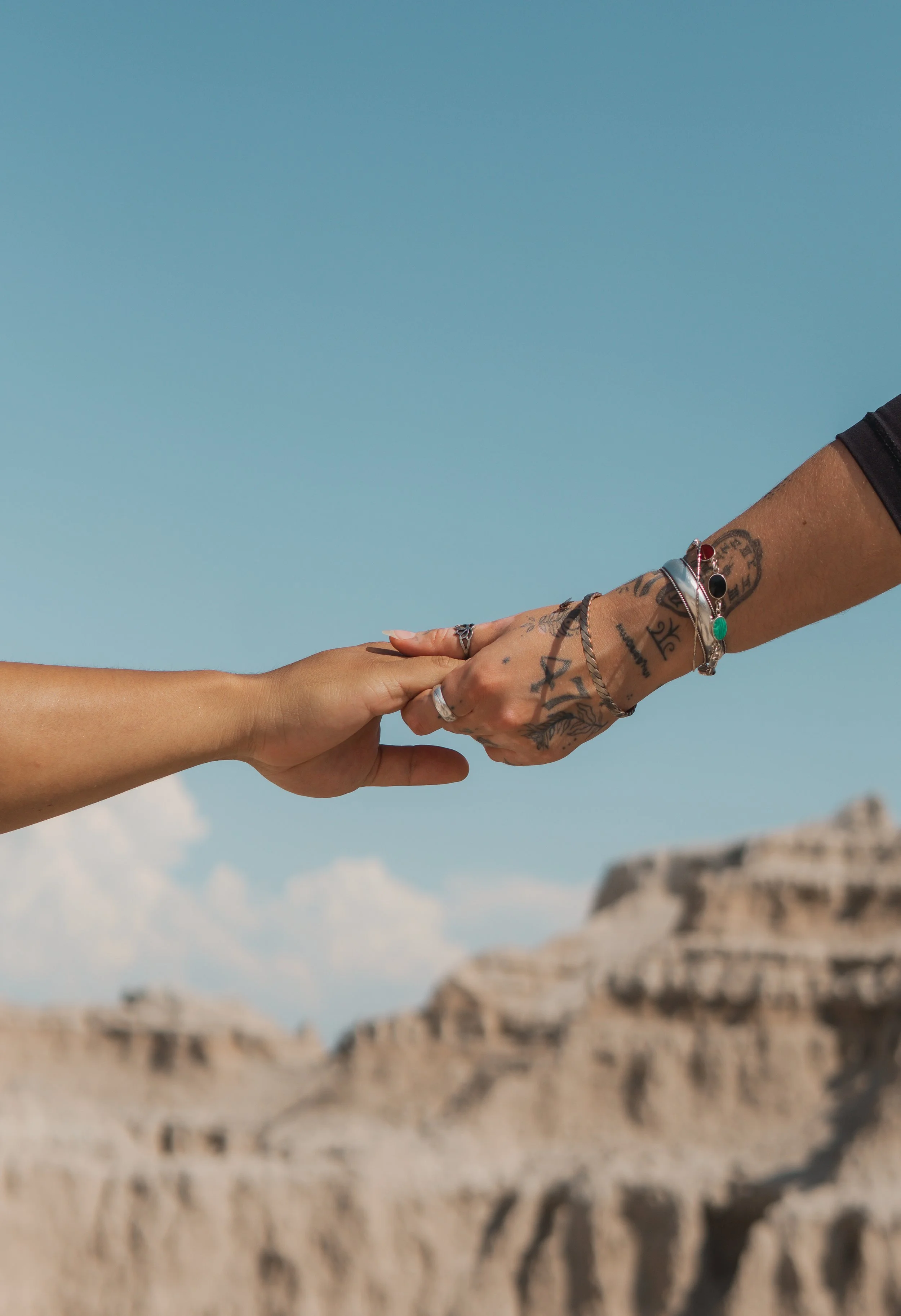 Two hands reaching out and holding each other against a background of the Badlands, Black Hills, SD under a blue sky.
