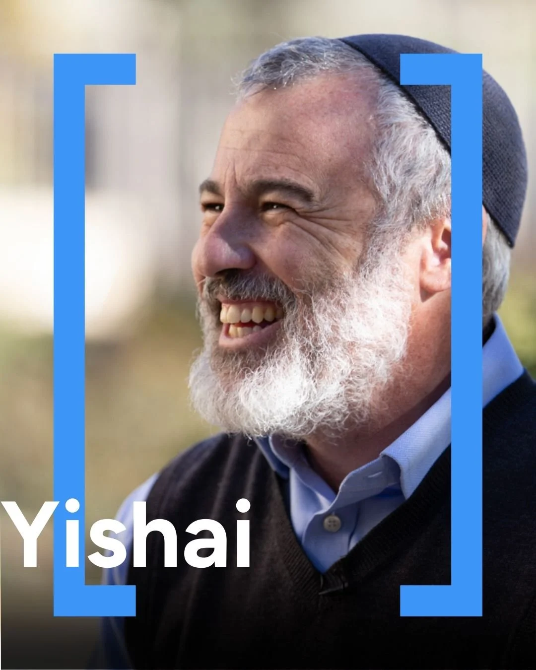 Smiling elderly man with gray beard and hair wearing a blue kippah and a blue shirt, outdoors, with the name 'Yishai' in white text at the bottom left corner.