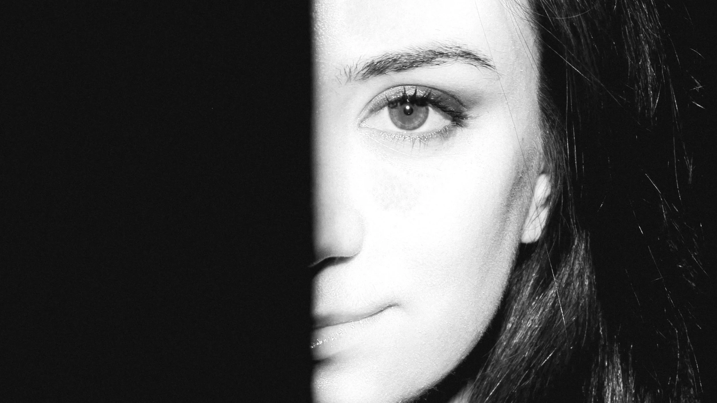 Close-up of a woman's face, half in shadow and half illuminated, with a focus on her eye and lips
