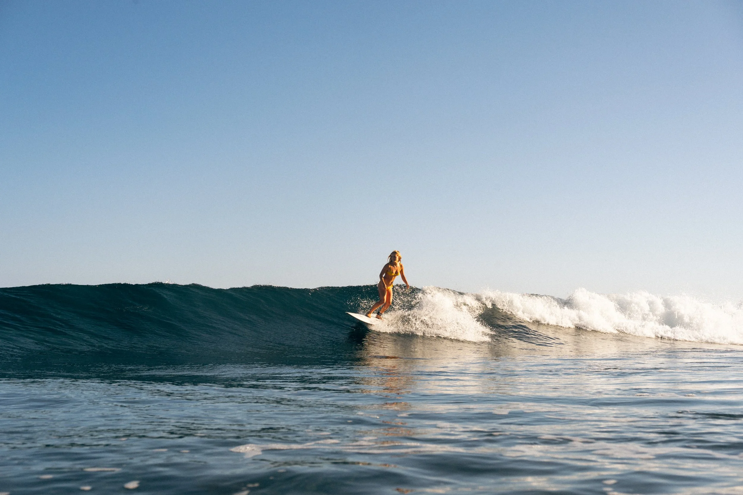 Woman surfing on a wave in the ocean under a clear blue sky.