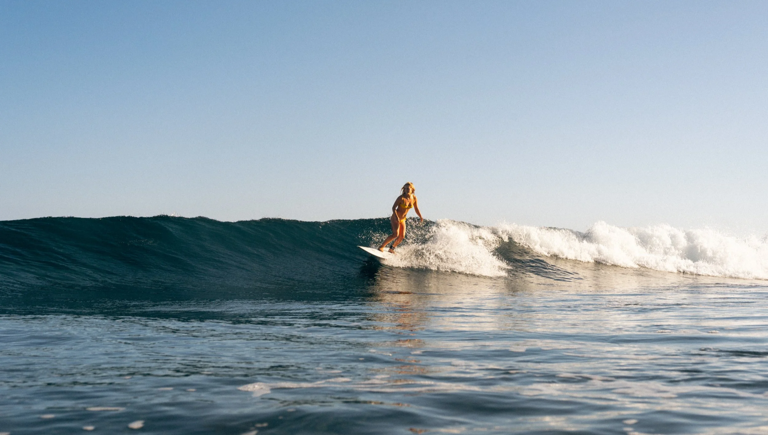 A woman surfing on a wave in the ocean under a clear sky.