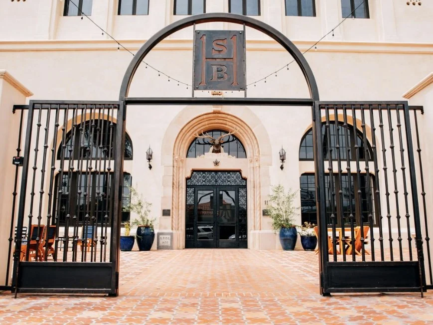 Entrance to a building with a large iron gate, stone archway, potted plants, and decorative lighting.