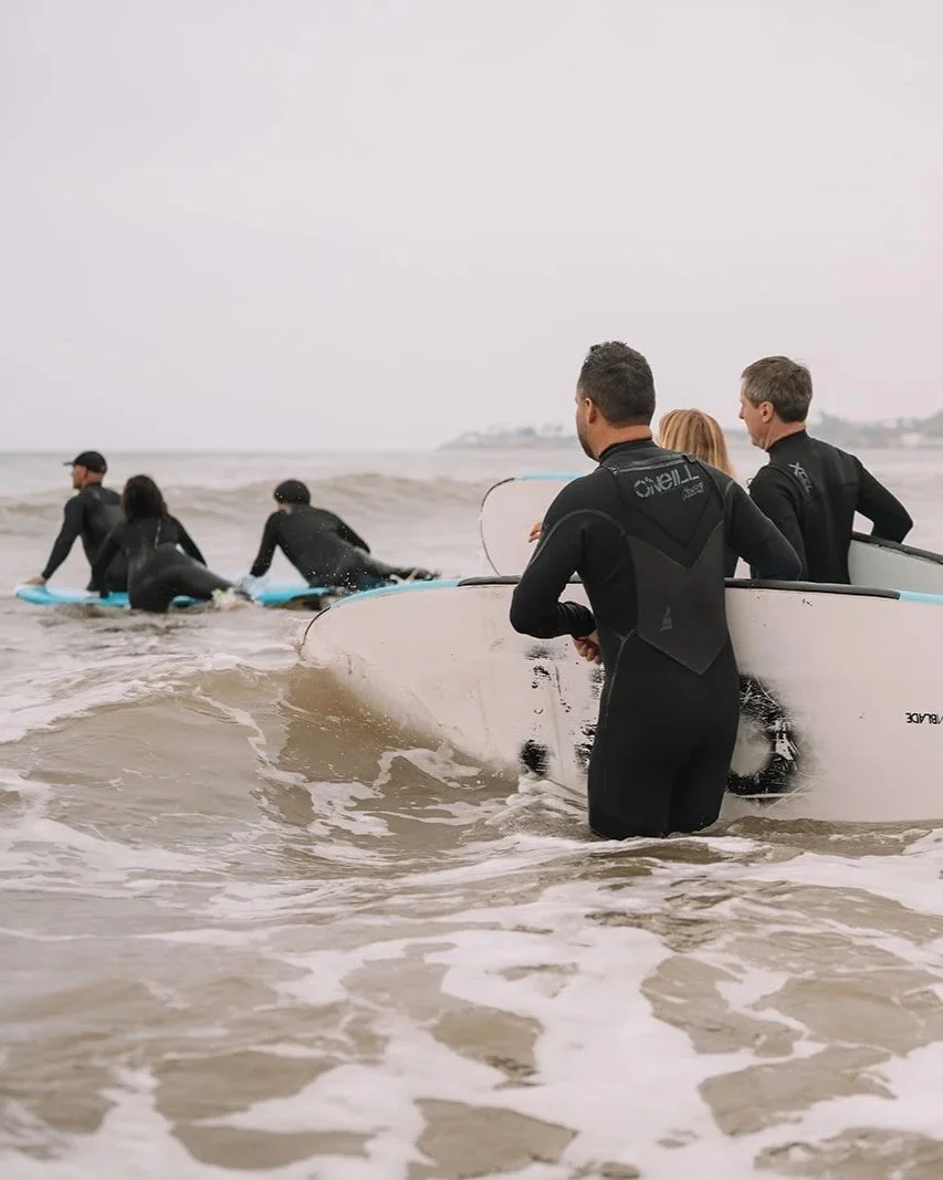 Group of people in wetsuits preparing to surf at the beach with surfboards in the ocean on a cloudy day.