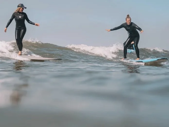 Two women in wetsuits surfing on a clear day