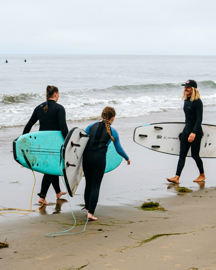 Three women with surfboards walking on the beach near the water, engaging in surf lesson or practicing surfing.