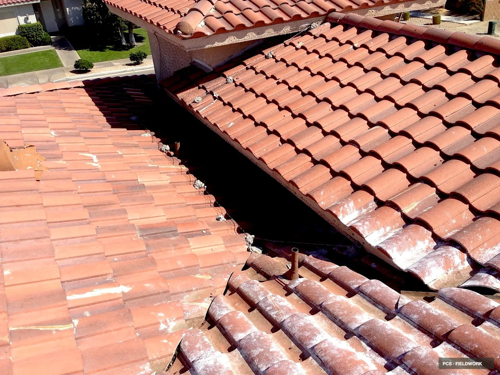 View of a roof with red clay tiles, showing areas with damaged or missing tiles, and some debris and construction materials on the roof.