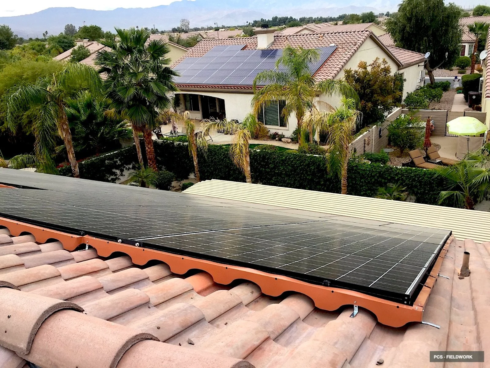 Solar panels installed on a tiled roof, with palm trees and a suburban backyard visible in the background.