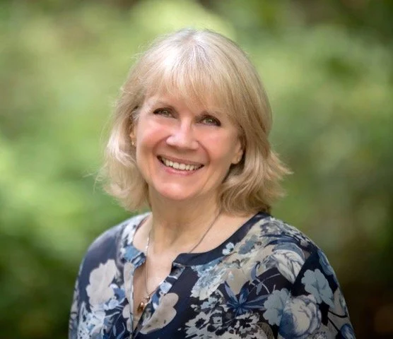Smiling woman with blonde hair wearing a floral blouse outdoors.