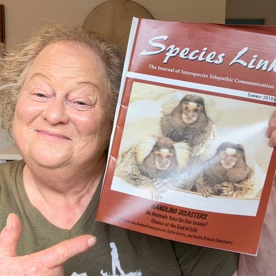An elderly woman with curly gray hair holding a magazine titled 'Species Link,' summer 2010 issue. The magazine cover features a picture of three monkeys and the headline 'Handling Disasters' at the bottom.