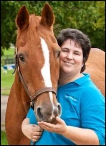 Woman smiling, holding a brown horse's face outdoors