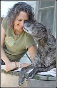 Woman and dog sharing a close moment, with the dog licking her face.